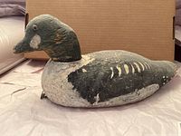 Side view of the wooden decoy duck showing the whole body, paint wear, and overall shape.