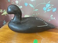 Side profile image showing the full body of the carved wooden decoy duck in dark brown with yellow beak and white wing detail on the tail.