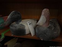 Pair of wooden duck decoys on shelf showing aged paint and wear