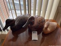Three assorted wooden decoy ducks placed on table showing size and grouping. Two large ducks carved from dark wood and one smaller light wood duck with paint wear and damage.