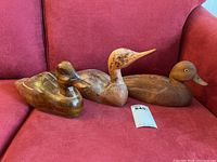 Three wooden duck decoys arranged on red sofa showing overall lot contents and size reference with lot tag.