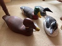 Four assorted wooden decoy ducks grouped on beige carpet, showing color and size variations.