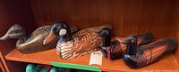 Four wooden painted duck decoys shown on a shelf, varying sizes and styles with naturalistic painting and visible wear