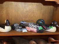 Four assorted wooden duck decoys displayed on a wooden shelf, showing various species styles and paint colors.