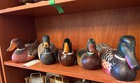 Five assorted wooden duck decoys lined up on a shelf showcasing varied colors and styles