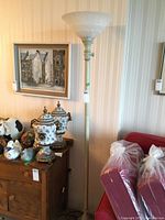 Full view of the tall metal floor lamp with frosted glass shade standing next to a dresser and couch.