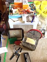 Wide photo showing assortment of jewelry, clocks and watches on floor including clocks stacked and wristwatches at front.