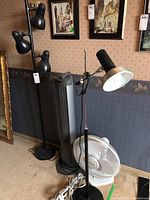 Full view of the two floor lamps, tower fan, and table fan together near a wall.