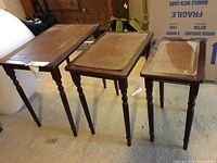Front view of three wooden nesting tables in descending size order, showing turned legs and worn leather-like inlays.