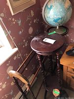 Photo showing wooden small pedestal table and blanket rack with globe in background, dark stained wood surfaces