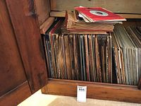 Records stored upright in a wooden cabinet with additional records stacked on top.