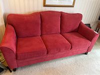 Front angle view of the red sofa showing three seat cushions and three back cushions, minor wear visible on fabric.