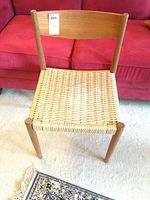Full front view of one chair showing teak frame and woven cord seat against red couch