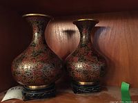 Pair of cloisonné vases with brass rims and black carved stands, showing the floral patterns and shape.