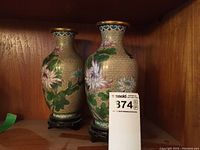 Front angle showing both floral cloisonné vases with wooden stands side by side on a wooden shelf.