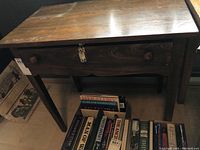 Full view of wooden table showing the drawer with a padlock and no key. Table legs and some books visible underneath.