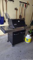 Front view of black Weber gas grill with side shelf, base cabinet with doors and wheels