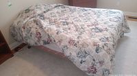 Bed with floral quilted comforter on top, showing overall setup and bed frame with side table in background