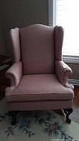 Front view of pink upholstered wingback chair with arm covers showing seat and arms.