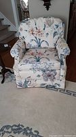 Front view of the upholstered living room chair showing floral fabric upholstery with pink, blue, and green flowers and leaves, cushioned seat and rounded armrests.