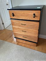 Front view of the wooden dresser showing the four drawers and wood/black color contrast.