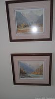 Photo of two framed prints hung on a wall, showing full frames and artwork on both paintings