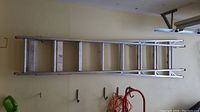 Full view of the entire aluminum extension ladder lying horizontally on a wall, showing its length and structure.