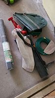 Items including Toro Ultra blower with carrying strap, Fiskars weed remover with red handle, white Scott's Turf Builder spreader with red handle, green garden hose rolled, and green bag.