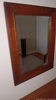 Rectangular mirror with wooden frame showing visible wood grain hung on wall above wooden surface, shelf not included.