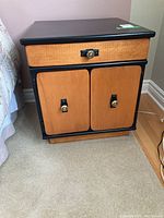 Front view of one nightstand showing wood finish drawer and two cabinet doors with brass knobs and black frame.