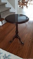 Angle view of dark wooden occasional table showing round top, pedestal, and one leg