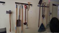 Full view of hanging garden tools: axe, spades, hoe, rakes, and small hand tools