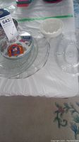 Multiple items on table including clear glass platters and small porcelain dishes with emblems.