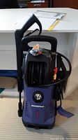 Front view of Simoniz blue and black pressure washer showing handle, hose reel, and sticker with brand name and model number.