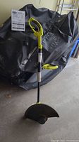 Electric yellow and black Ryobi string trimmer/edger leaning against a covered object, showing full length, handle, guard, and cutting head.
