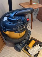 Rona 10 gallon 6.5 hp wet/dry shop vac with hose coiled around the unit and blower accessories nearby.