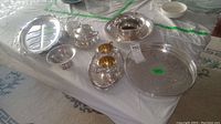 Wide layout image of silver plated assortment on table showing multiple trays, bowl, cream and sugar cups, and coasters.
