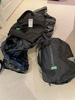 Photo of two deflated black air mattresses alongside two black fabric carrying bags on beige carpet.