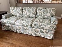 Full front view of the 3 cushion floral sofa on wooden floor.