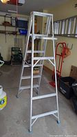 Full view of the aluminum step ladder standing open in a garage, showing its structure and steps.