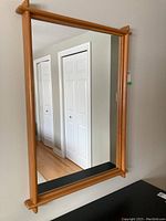 Full view of the wooden framed wall mirror mounted on the wall reflecting a hallway with white doors.