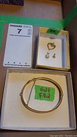 Photo of gold filled hinged bangle bracelet with floral engraving and three 10K gold pendants (heart, snowflake, pearl) in a box with labels indicating gold content.