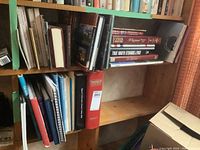 Photo of bookshelf with various history and reference books including 'TrueNorth Strange & Free' and large red Chronicle binder.
