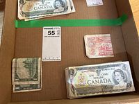 Overview of currency including folded 1974 two dollar bill, folded 1967 one dollar bill and stack of 1973 one dollar bills.