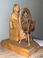 Side view showing the full figure of the woman at the spinning wheel with chair and base visible.