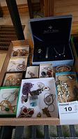 Wide shot of multiple trays and boxes containing assorted costume jewellery pieces including necklaces, rings, earrings, and watches.