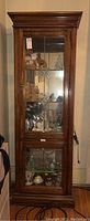 Front view of the tall wooden display cabinet showing glass door with beveled glass panels and contents inside.