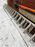 Two aluminum extension ladders leaning against a brick wall in snow