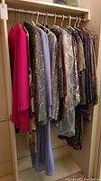 Side view of assorted womens formal jackets, blouses, dresses, and kilts hanging on hangers in closet space