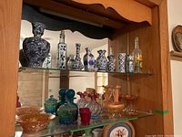 Full view of glass cabinet shelf showing various blue and white ceramic vases, colored glassware, and carnival glass items.